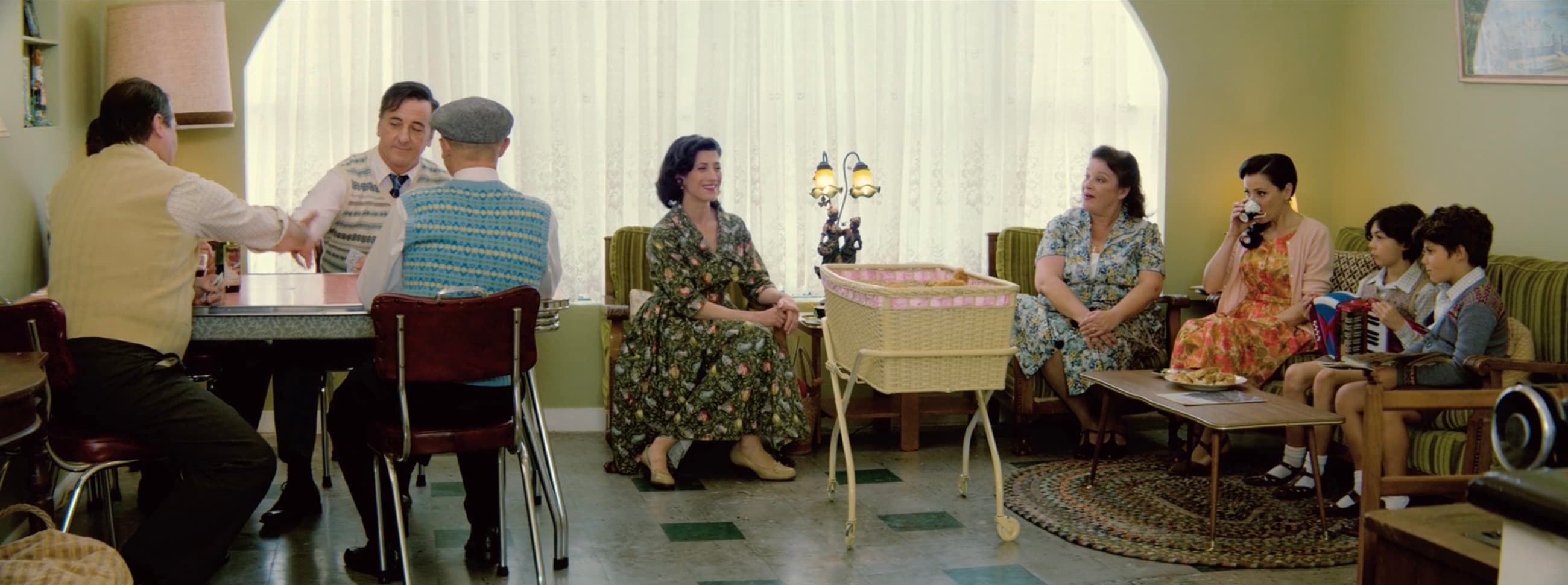 Two families in a Melbourne living room in 1953; the fathers shake hands across the table while the baby sleeps in her bassinet.